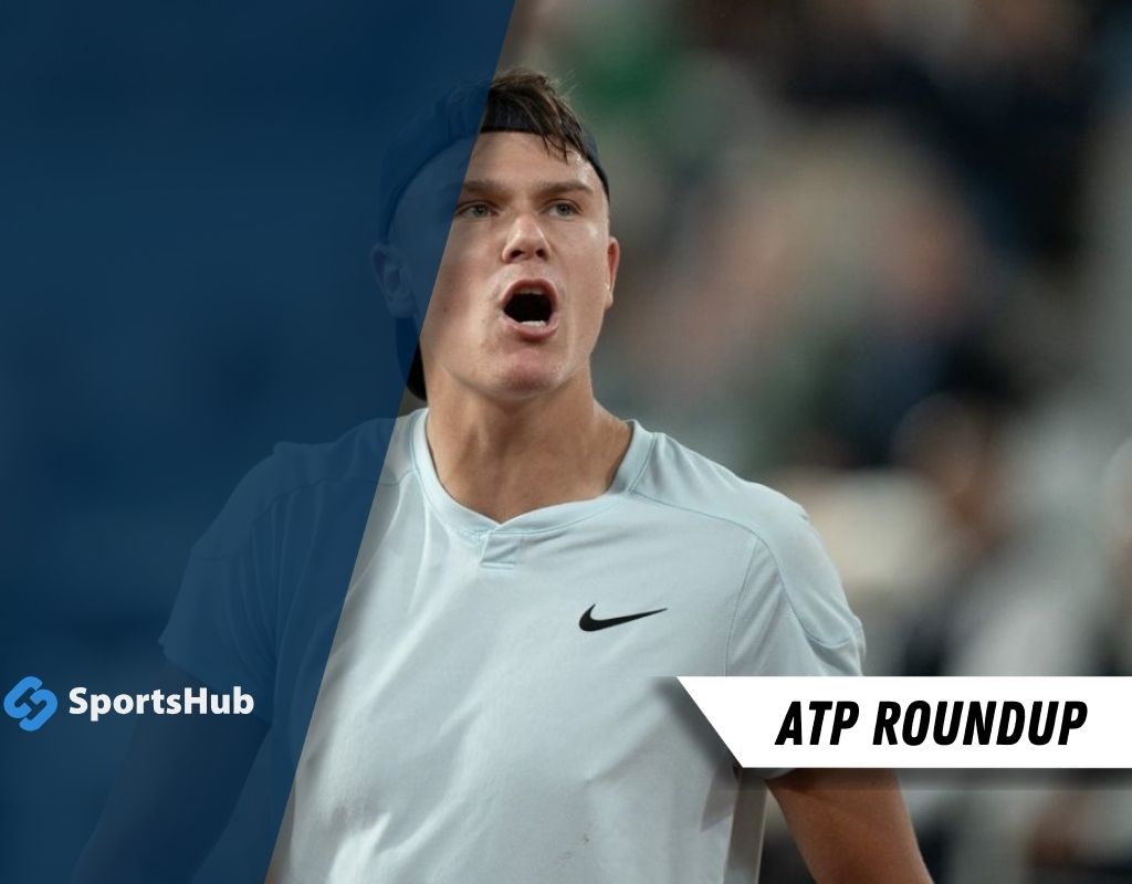 A tennis player in a light blue Nike shirt walks on the court, with a blurred background and the text "ATP Roundup" visible.