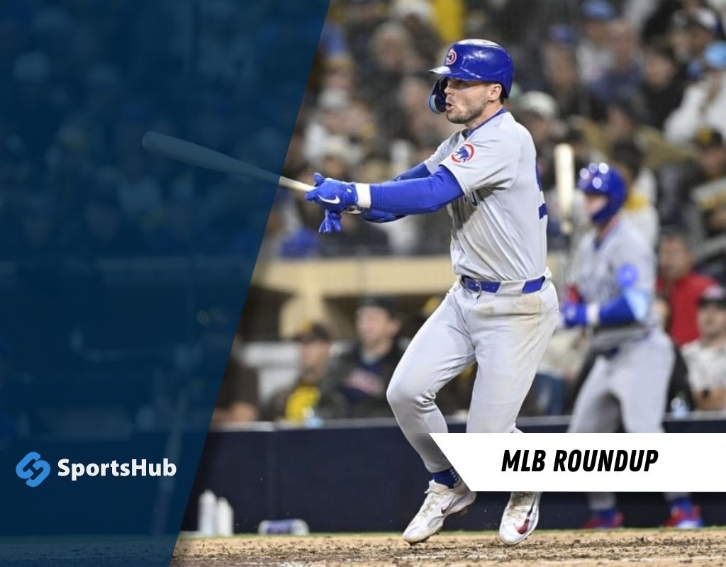 A baseball player in a blue and gray uniform swings a bat during a game, with cheering crowds visible in the background.