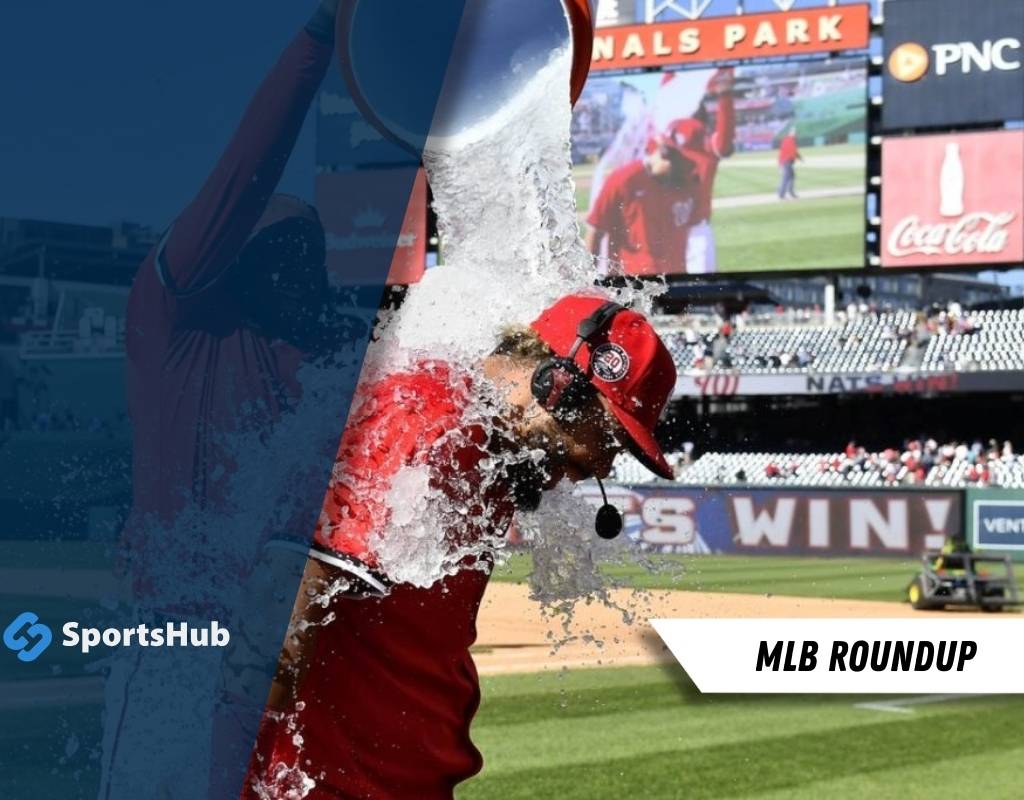 A Nationals player gets doused with water in celebration at Nationals Park, with a game highlight displayed on the big screen behind.