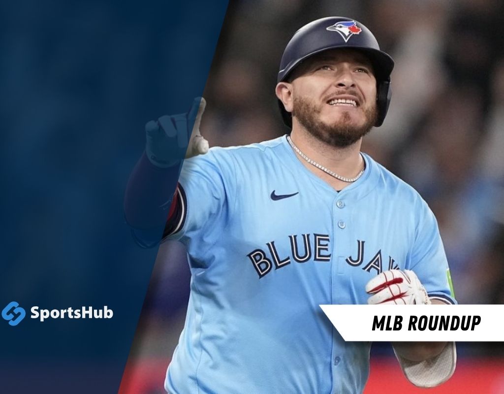 A baseball player in a light blue jersey with "BLUE JAYS" printed on it gestures during a game, with a "MLB ROUNDUP" graphic overlay.