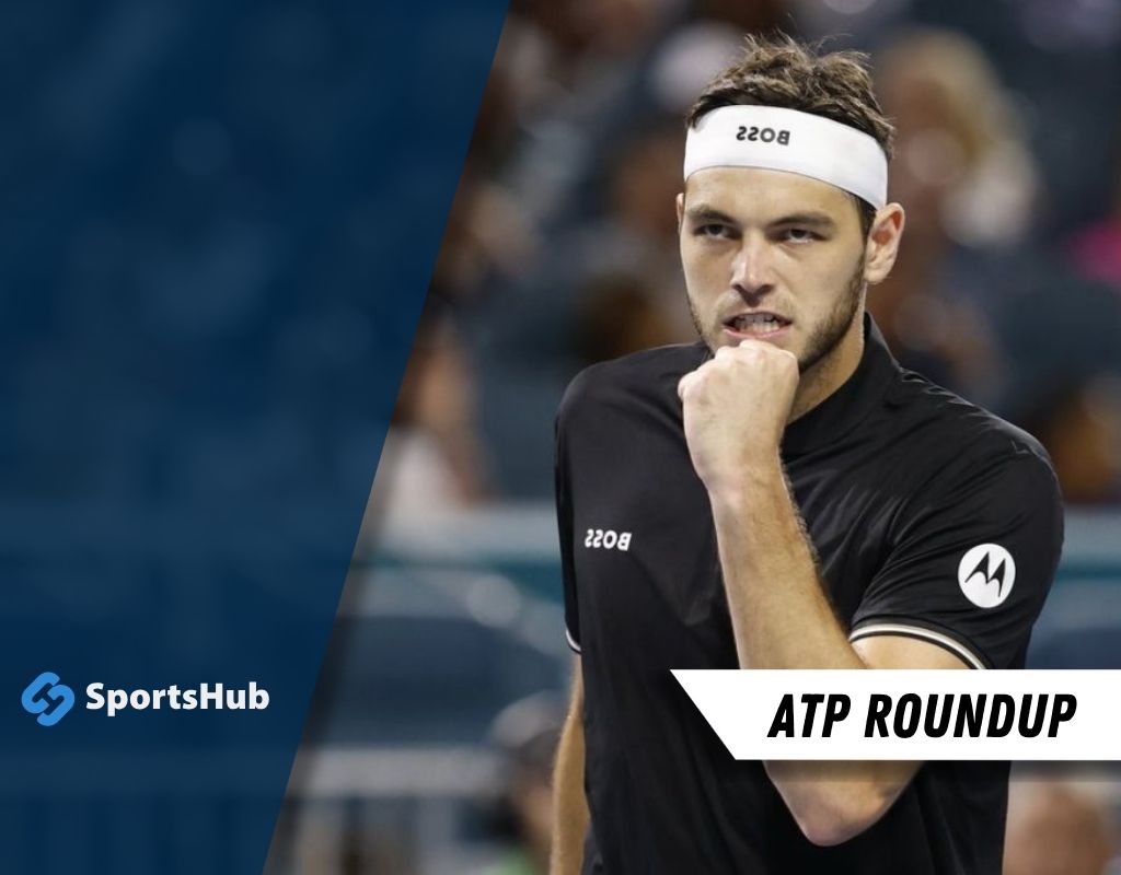 A tennis player in a black shirt and white headband gestures during a match.