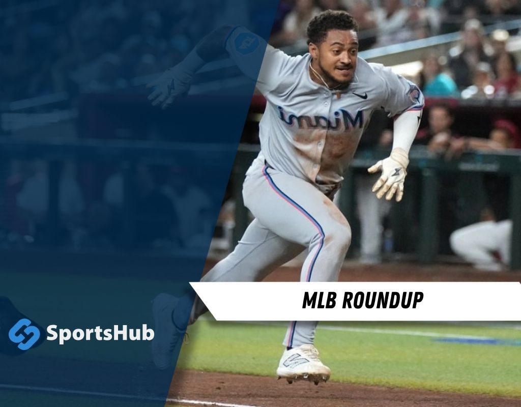 A baseball player in a gray uniform sprints toward first base during a game, with spectators visible in the background.